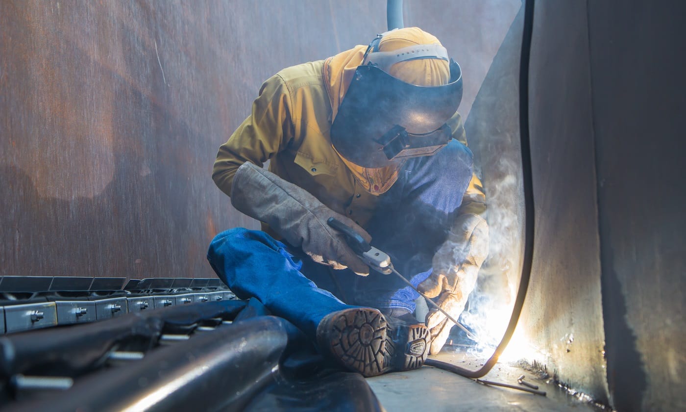 Male worker wearing protective clothing and repair welding plate industrial construction oil and gas or storage tank inside confined spaces.