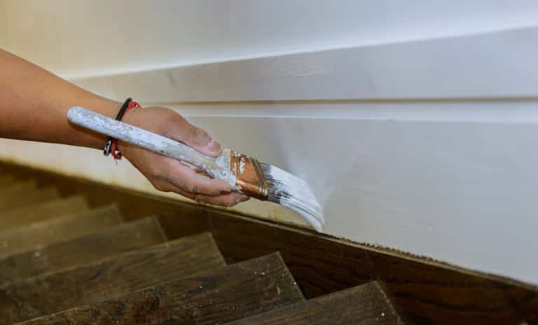 Working contractor painter hands with painting the wood molding trim on stairs with brush