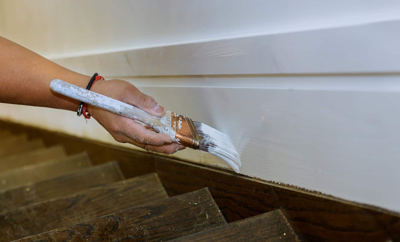 Working contractor painter hands with painting the wood molding trim on stairs with brush