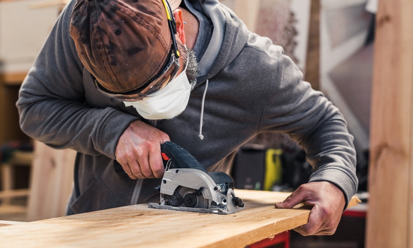 Carpenter with face mask cutting a plank of wood with a electric circular hand saw. ROCKWELL VersaCut RK3440K Mini Circular Saw