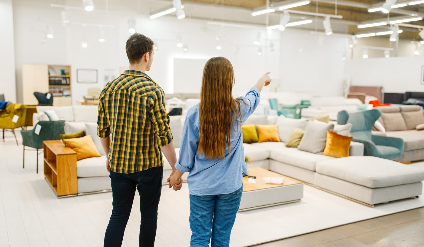 Happy couple choosing furniture in store showroom. Man and woman looking samples for bedroom in shop, husband and wife buys goods for modern home interior