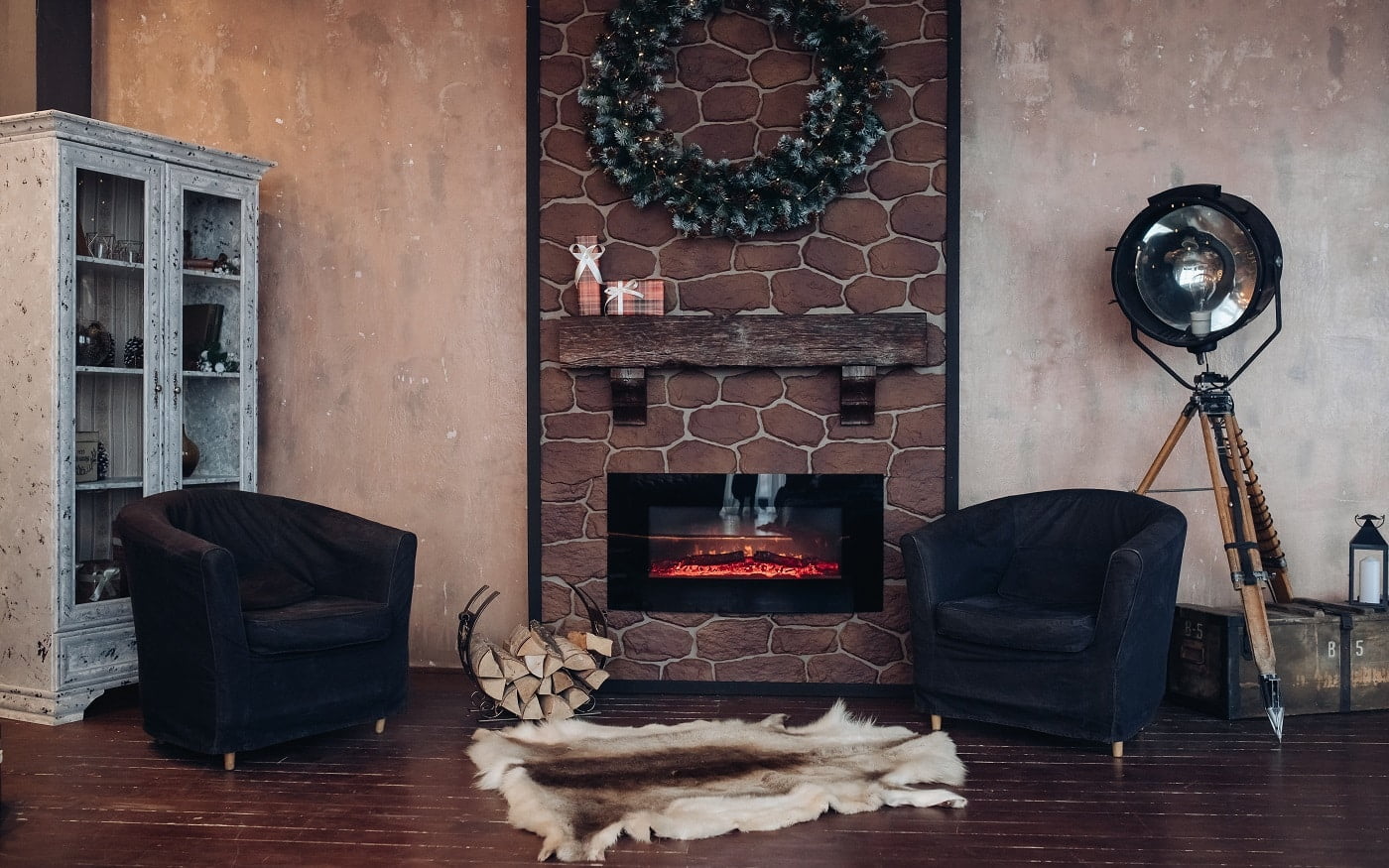Christmas interior decorated with Christmas wreath made of fir branches. Two armchairs and a genuine animal fur on the floor in front of an electric fireplace.