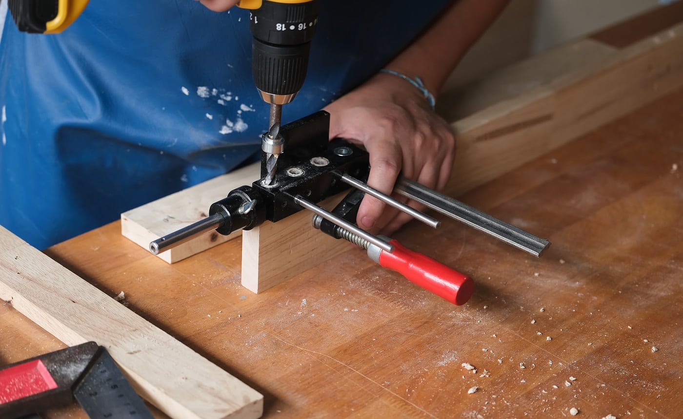 Woodworking entrepreneurs are using a drill through the wood holes to assemble and build wooden tables for customers.