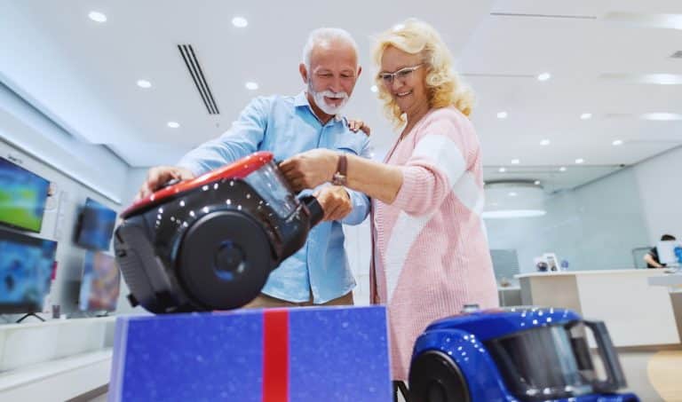 Cute Caucasian senior couple choosing new vacuum cleaner for their home. Tech store interior.