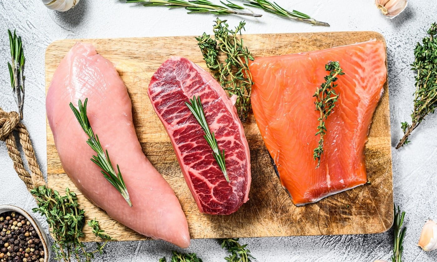 Different types of raw meat on cutting board with herbs. Beef top blade, salmon fillet and Turkey breast. steaks. White background. Top view.