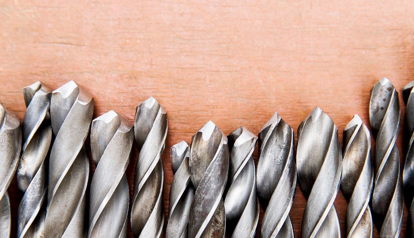 Set of old various twist drill bits with different sizes on wooden background, close up, top view, copy space.
