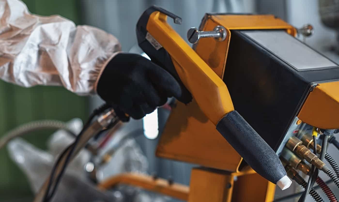 Hand of a worker wearing a protective wear holding powder coating sprayer in a metal producing factory