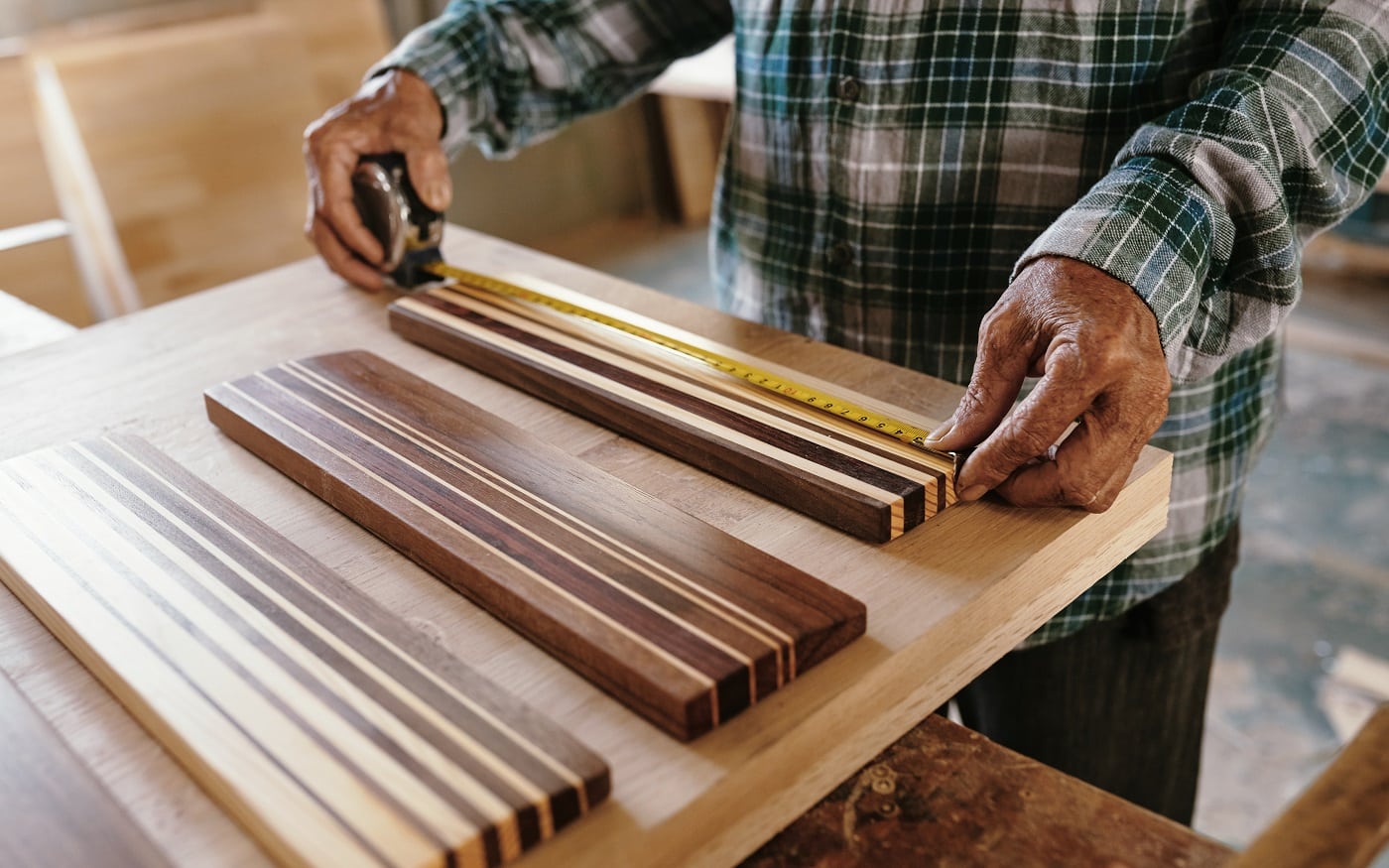 Hands of elderly carpenter measuring walnut and maple wooden pieces fused together for making edge grain cutting board