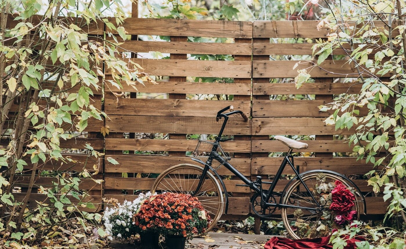 Vintage wooden fence covered with autumn leaves and a bicycle standing nearby at the autumn yard. Seasons concept. Stock photo