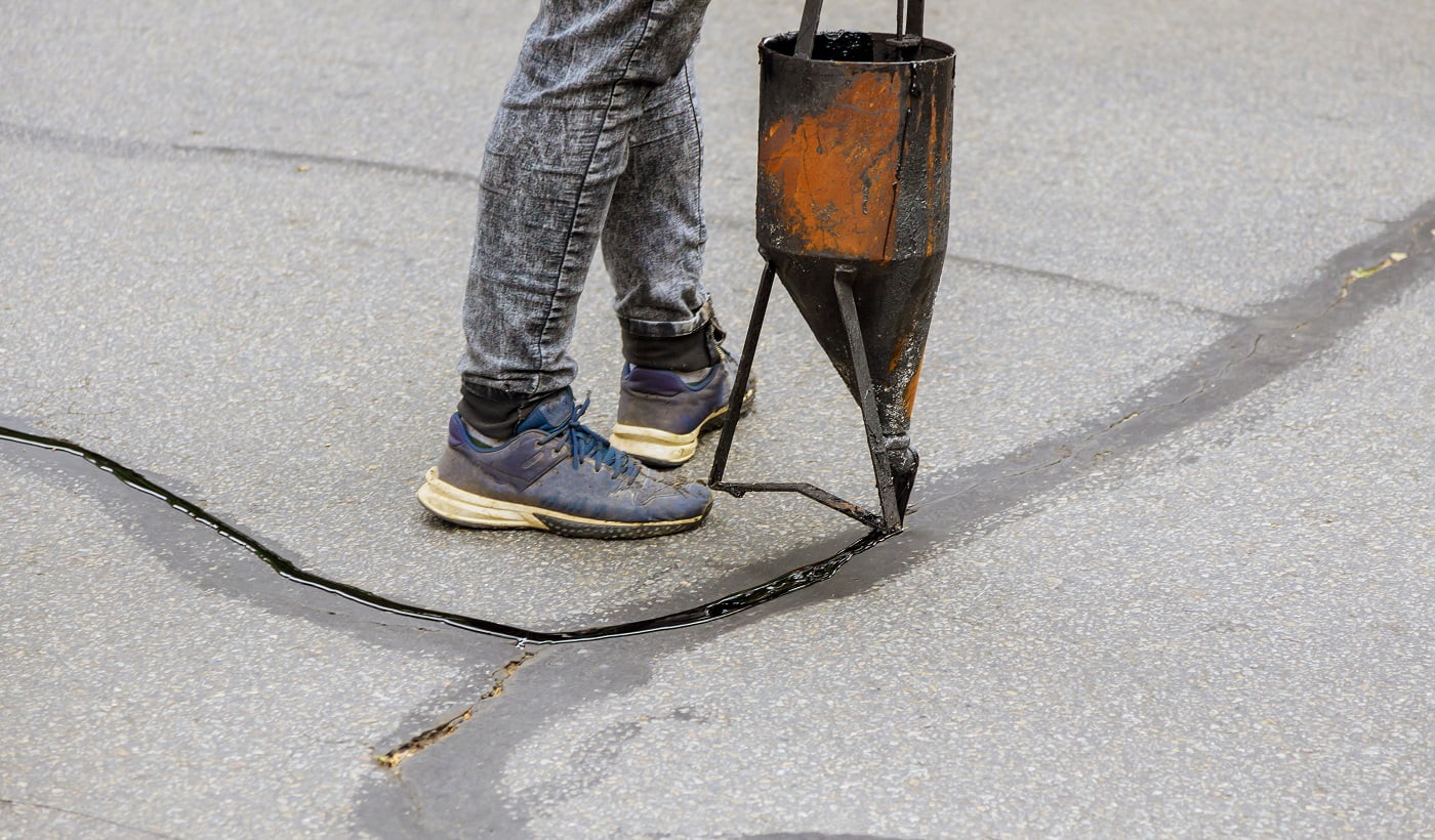Workers restoration work sealing cracks applying liquid sealer to asphalt a road protective coat on roadway