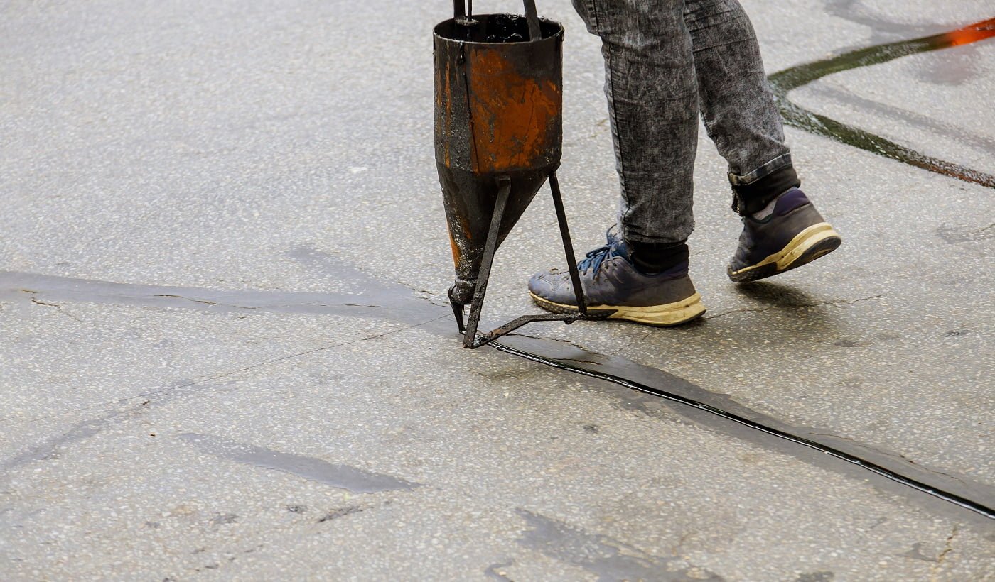 Workers applying blacktop sealer to asphalt a road protective coat restoration work. Driveway Sealer Buyer’s Guide