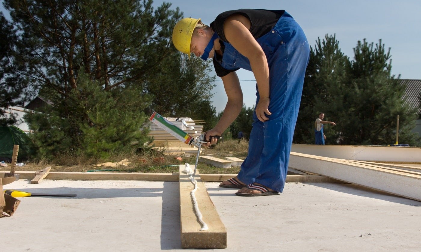 Builder or carpenter applying glue to a wooden beam on a construction site from a glue gun