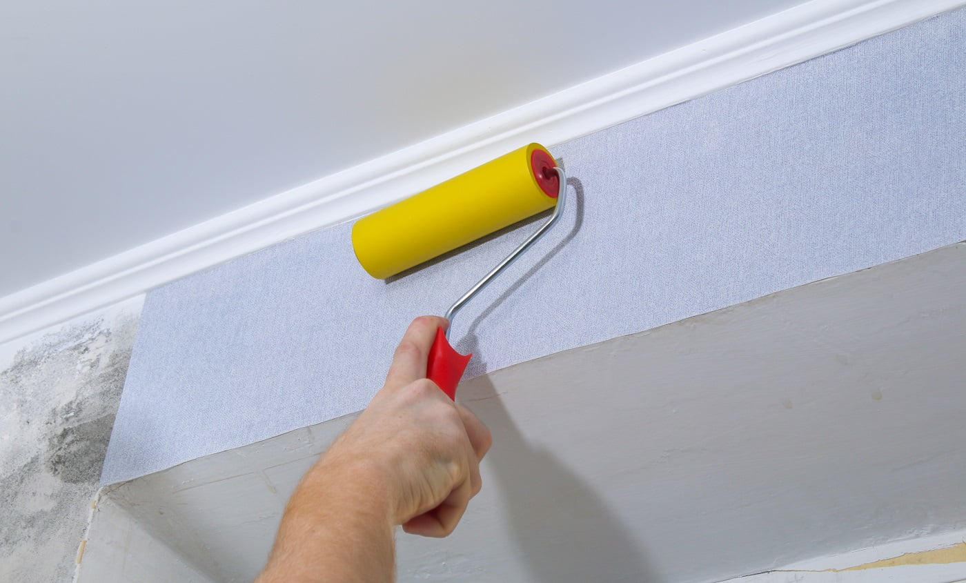 A man glues gray vinyl wallpaper on a non-woven backing. Renovation of the room.