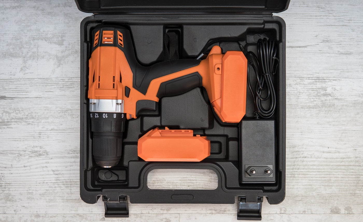 Top view of electric screwdriver on white background. orange screwdriver or drill in a black container lies on the floor. Tool for tightening screws. screw gun