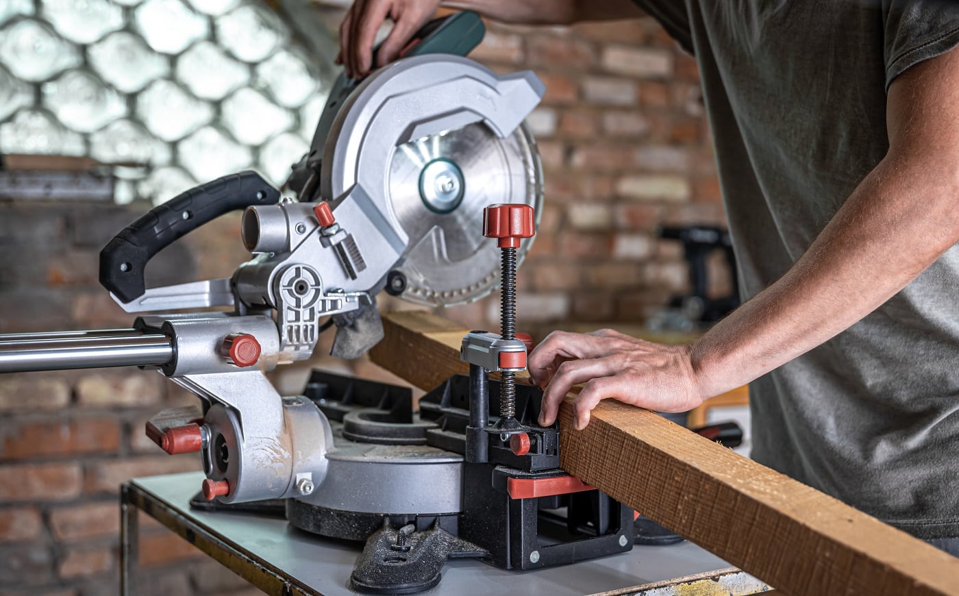 A man with a board and miter saw close up, concept building and repair.