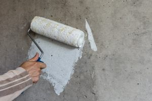 A painter paints a concrete wall with white paint, a male hand with a paint roller for painting a wall
