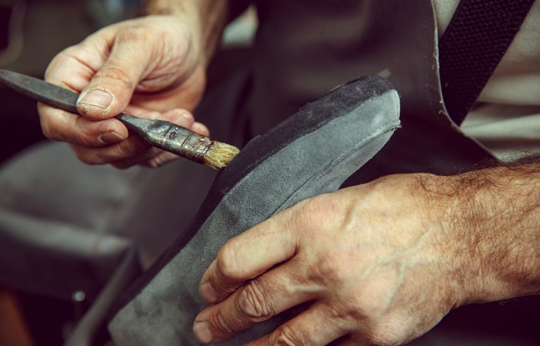 Shoemaker makes shoes for men.He smears special liquid with a brush.