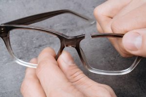 Closeup of man's hands holding broken frame of glasses. Young optometrist holding in his hands recked eyeglasses ribs. Professional repair of broken glasses in optician clinic.