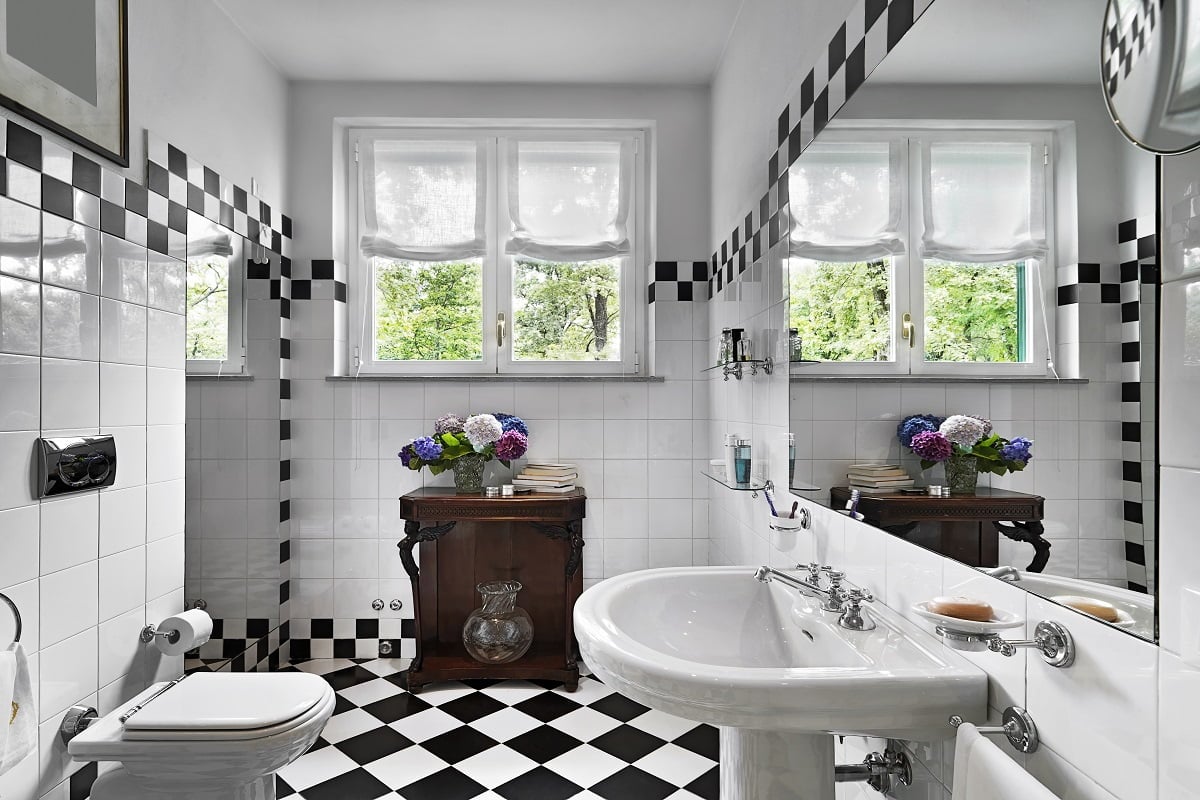 modern bathroom interior with black and white tiles in the foreground on the right the column sink while in the background an old cabinet with a vase of flowers on it