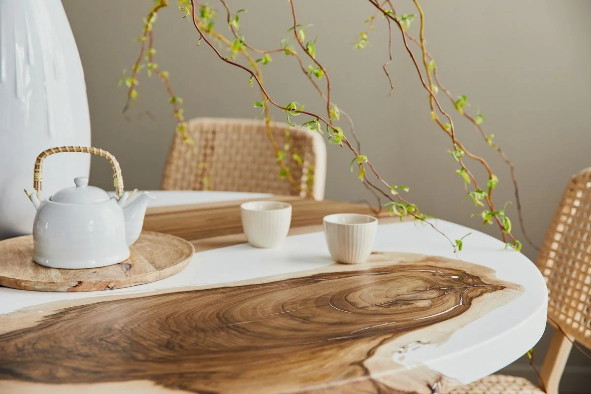 Interior design of stylish dining room interior with family wooden and epoxy table, rattan chairs, flowers in vase and teapot with cups. Details. Template.