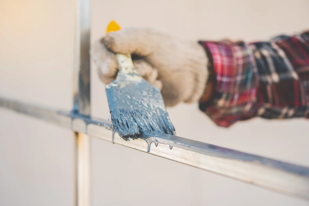 hand holding the brush is painting the iron fence to prevent rust