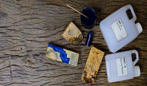 Mixing color blue epoxy resin in a glass cup for casting burl wood on old wooden background