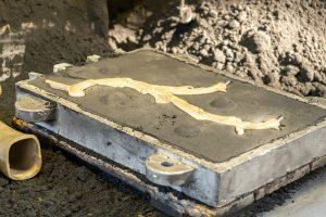 Decorative metal branch detail molded in form on pile of grey powder in light production plant workshop extreme close view