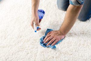 cleaning and home concept - close up of male cleaning stain on carpet with cloth