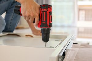 man assembling white table furniture at home using cordless screwdriver