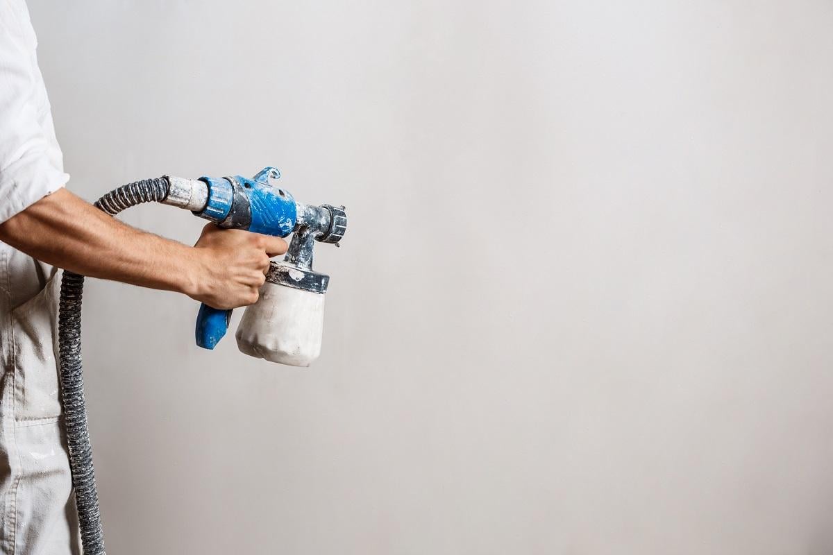 Worker painting wall with spray gun in white color. Copy space.