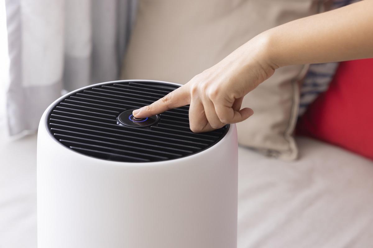 Close-up Asian woman hand, pressing a button on air purifier machine in a bedroom. Protect PM 2.5 dust and air pollution concept. air cleaner removing fine dust in house.