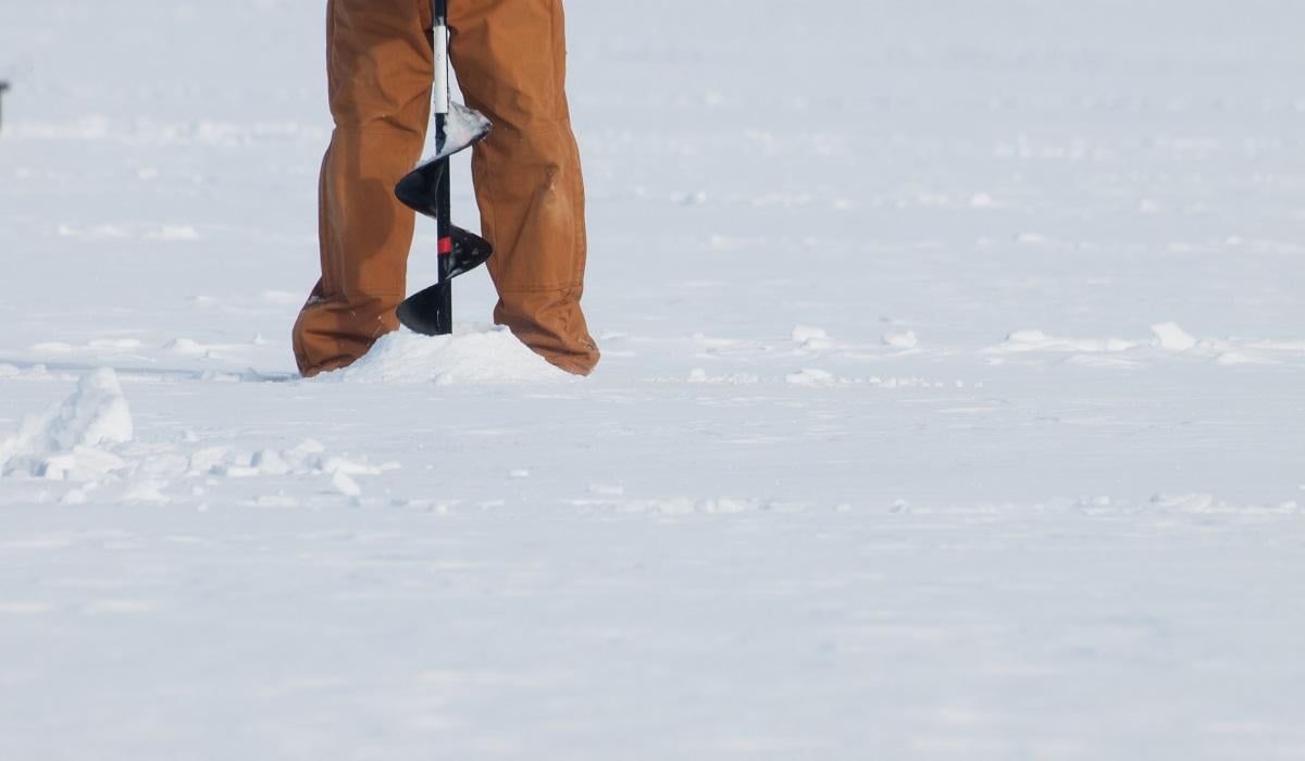 Fisherman with an auger on the frozen lake Granby, Colorado.
