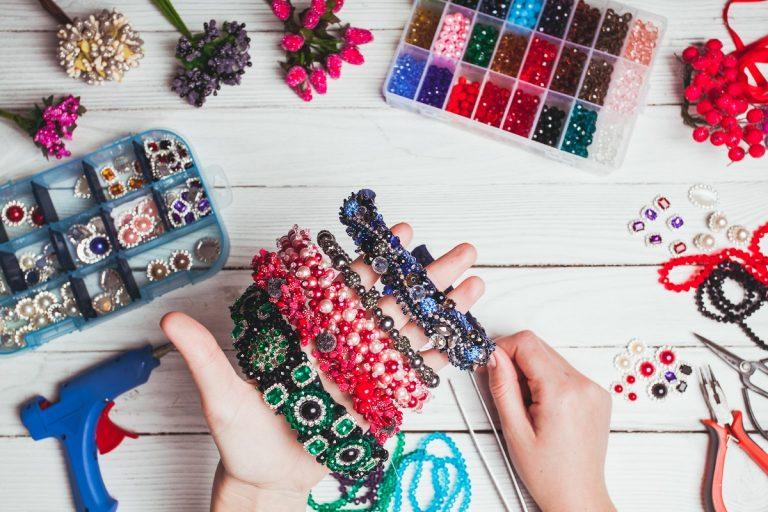 Plastic berries, flowers, beads and instruments for doing handmade headbands. Top view with hands