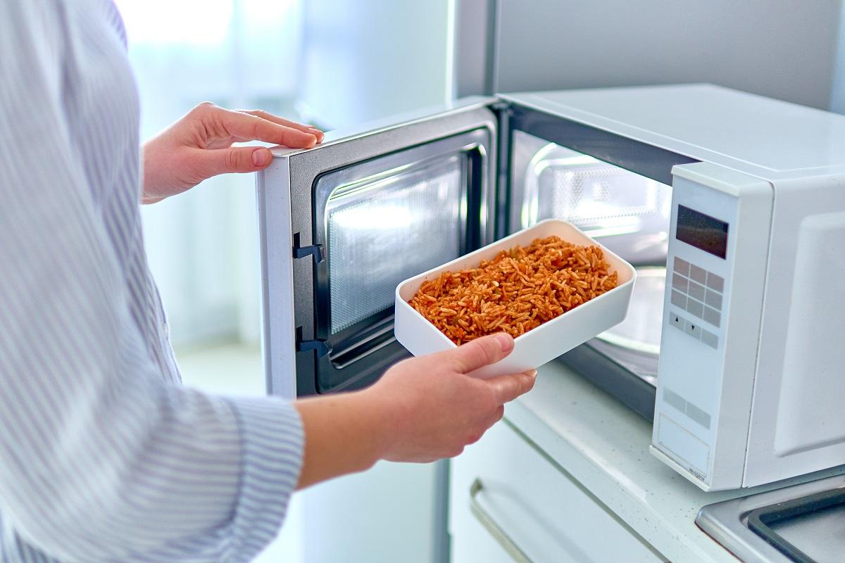 Female hands warming up a container of food in the modern microwave oven for snack lunch at home with the best microwavable dishes