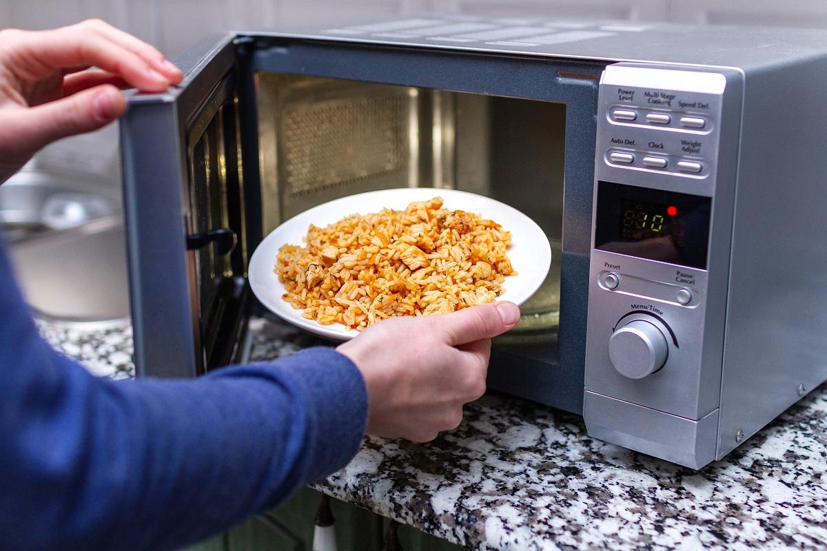 Using a microwave to warming a plate of homemade pilaf for lunch at home. Hot meal