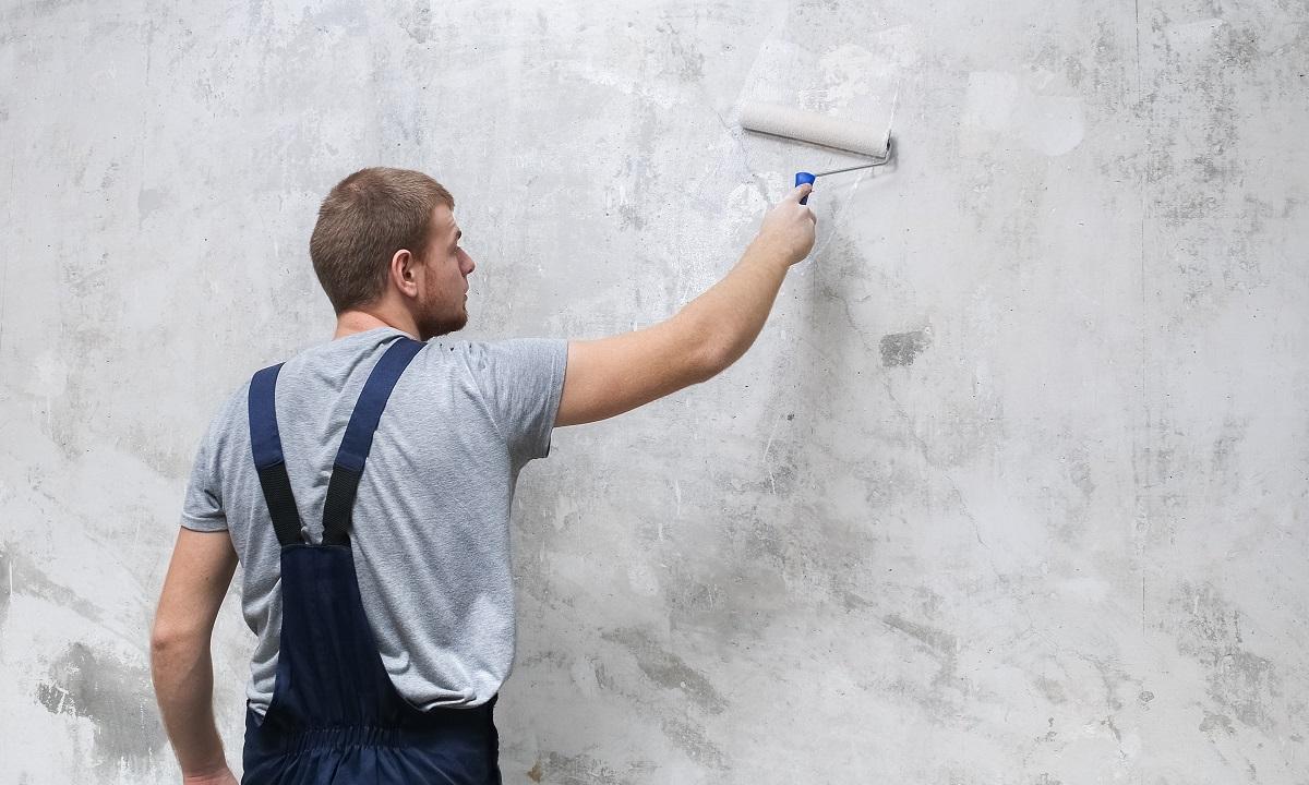 A male worker primes the wall with a roller for better grip.