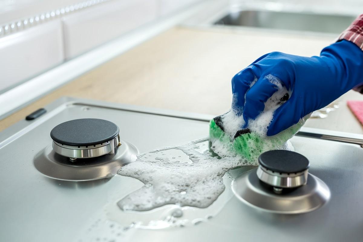 Woman with sponge and rubber protective glove used to wipe down an oven range top