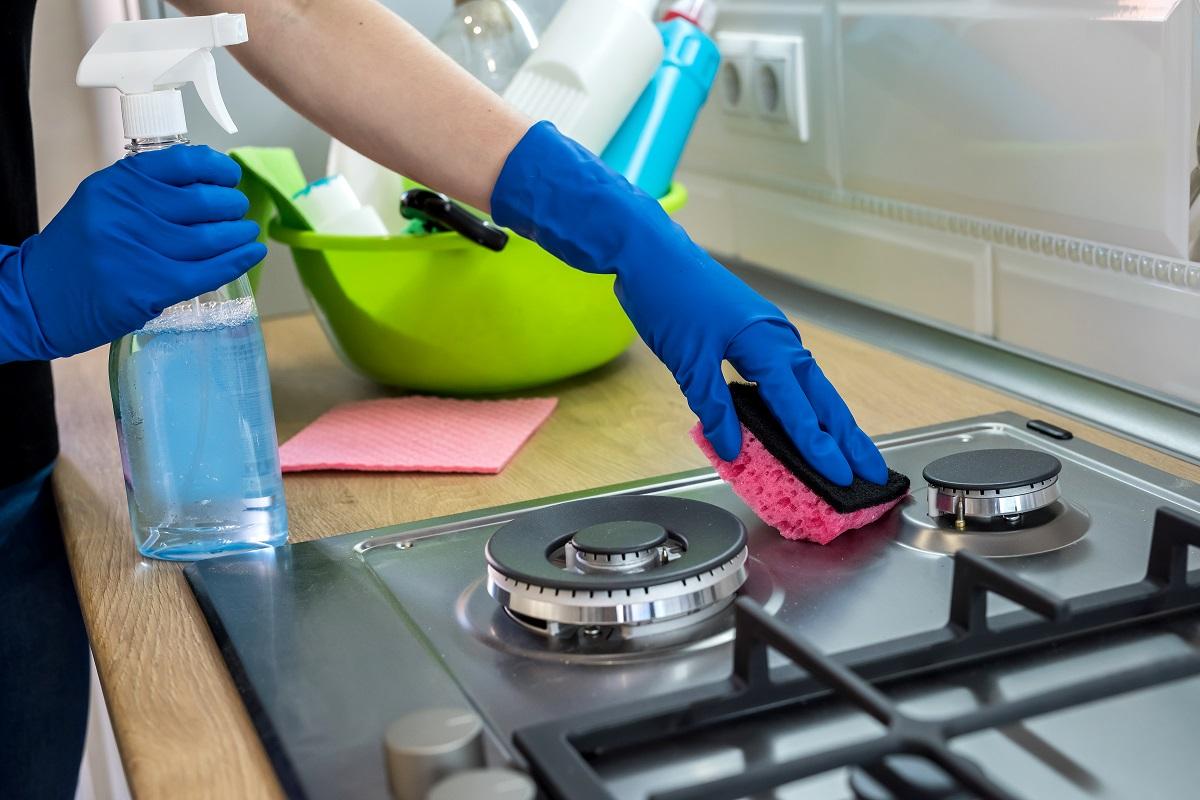 Woman cleaning stainless steel gas surface in the kitchen with rubber gloves and Oven Cleaners 