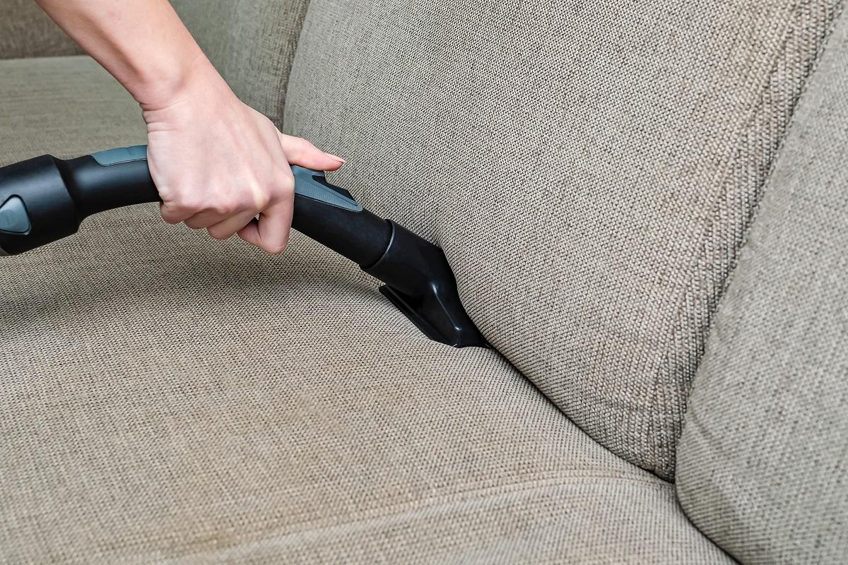 woman vacuums the gray sofa with a washing vacuum cleaner. Cleaning and cleanliness concept.