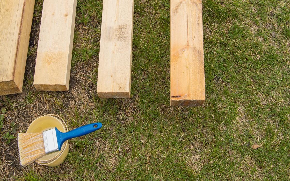 Preparation for painting new wooden boards lying on the grass, a paint brush with a bucket.