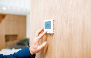 Adjusting room temperature with electronic thermostat at home, close-up view with no face