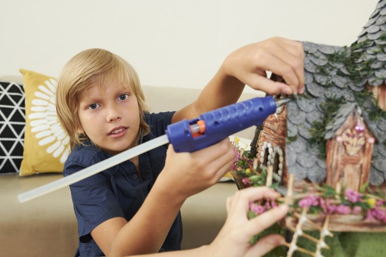 Creative preteen boy with glue gun making roof of fairytale castle with pieces of felt. Glue For Felt