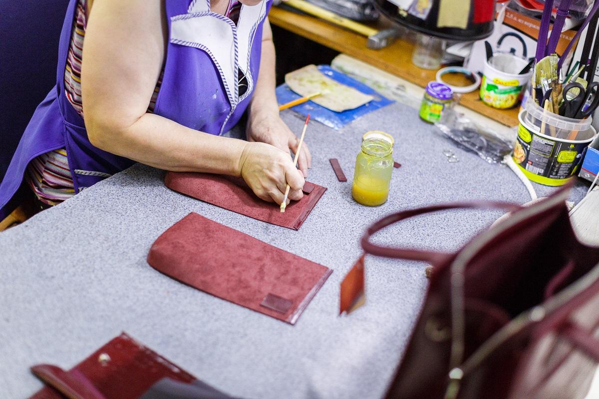 woman in dark-blue uniform smearing with glue a part of burgundy handbag. How Do You Glue Two Pieces of Leather Together.