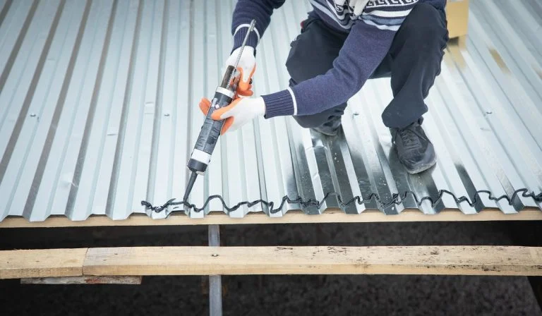 Worker using glue gun with adhesive to fix the metal steel on the roof. Heat Resistant Glue For Metal.