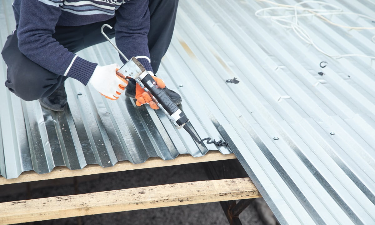 Worker using glue gun with adhesive to fix the metal steel on the roof. Heat Resistant Glue For Metal.