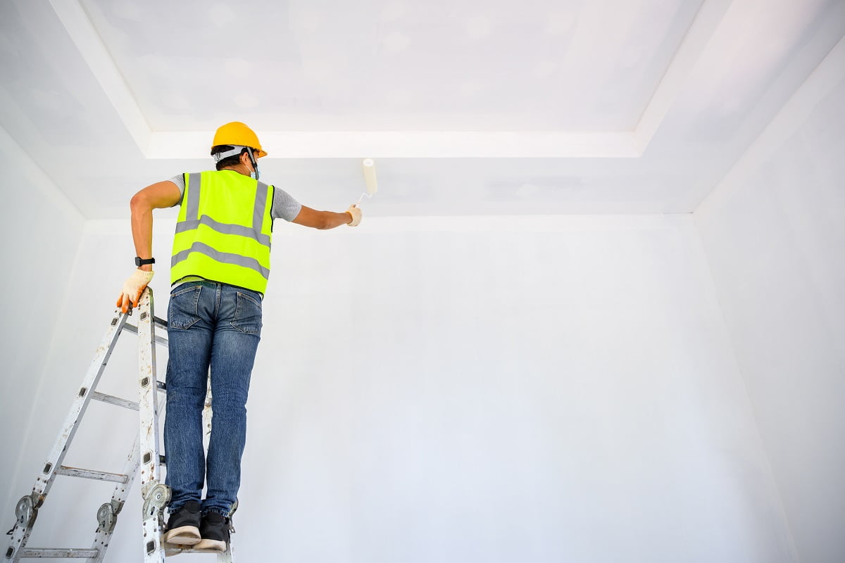 Young Asian male construction worker Work as a house painter Painting the ceiling inside the house and using a white primer paint roller on the construction site. Tips For Painting The Ceiling With A Roller.