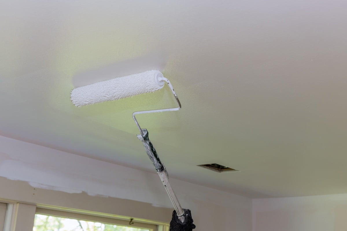 Rear view of painter paints the ceiling with a roller in room. How To Paint A Ceiling With A Roller Frequently Asked Questions.