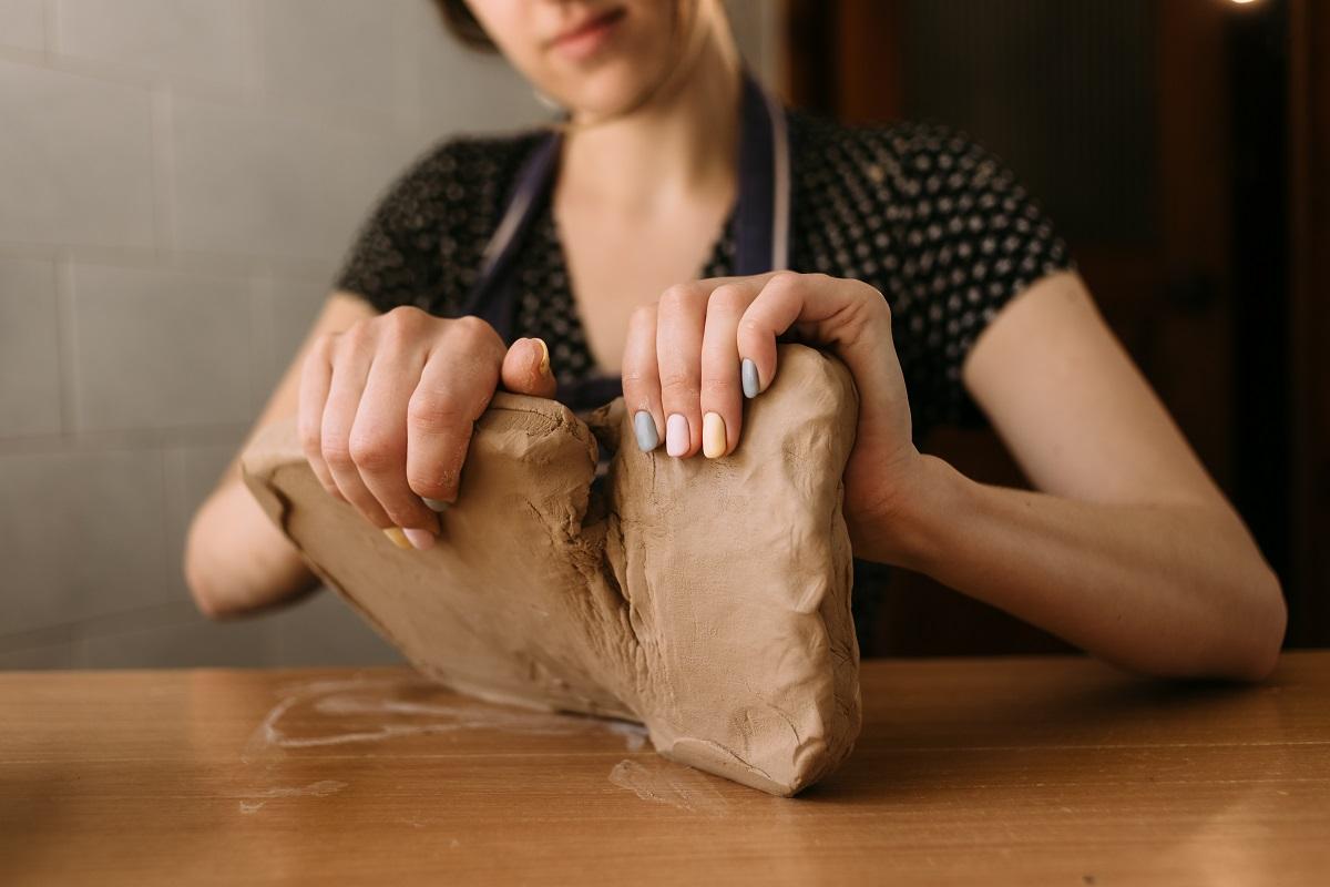 Close-up of the female hands of a potter, begins to make a product from clay, takes a large piece of material and divides it into two parts. Copy space. Beginner Sculpting Clay.