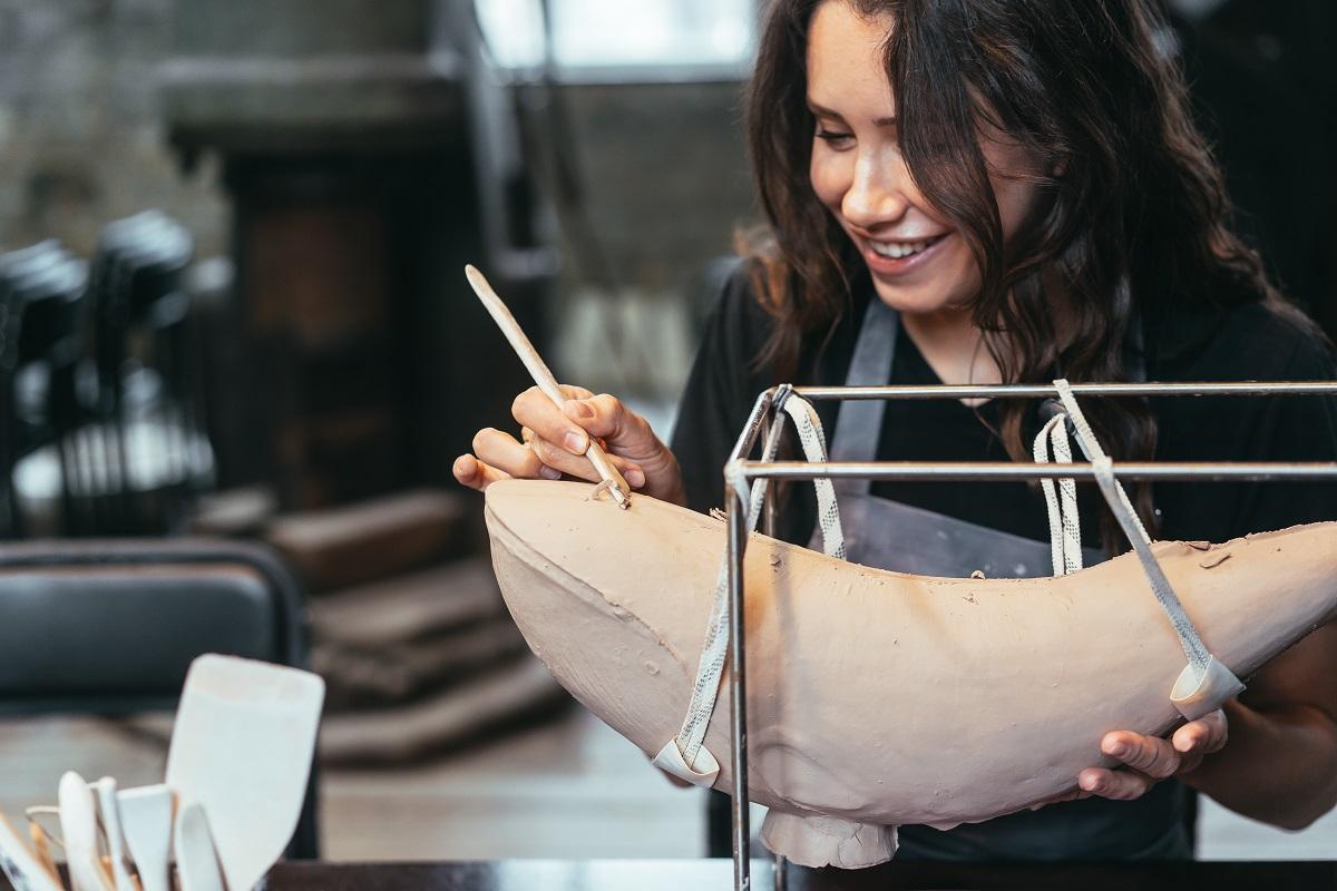 Portrait of young woman enjoying favorite job in workshop. The potter carefully works on the clay whale. Clay Modeling Ideas.