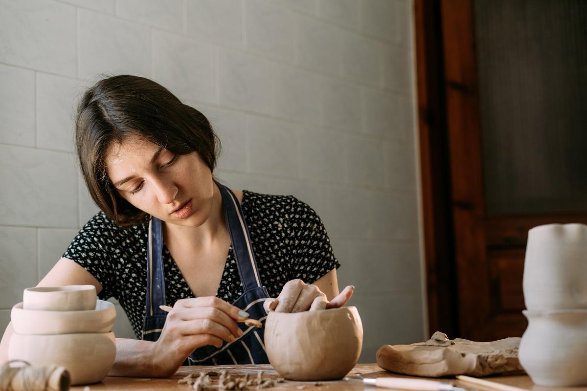 An Armenian girl makes a clay product. Modeling in a home workshop. Creativity and handmade. Clay pot in the hands of a woman with a tool. Art and texture concept. Clay Pots.